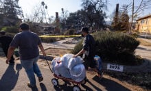 People pull a wagon of items through a neighborhood where many homes were destroyed by the Eaton Fire on January 11, 2025 in Altadena, California