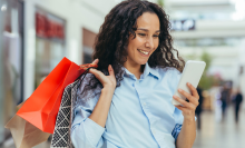 Woman in mall looking at her mobile phone while holding shopping bags