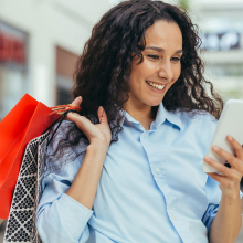 Woman in mall looking at her mobile phone while holding shopping bags