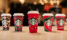 five starbucks red cups with various holiday designs lined up on a counter