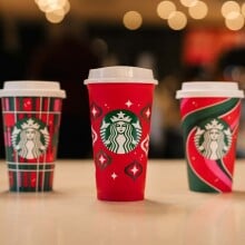 five starbucks red cups with various holiday designs lined up on a counter