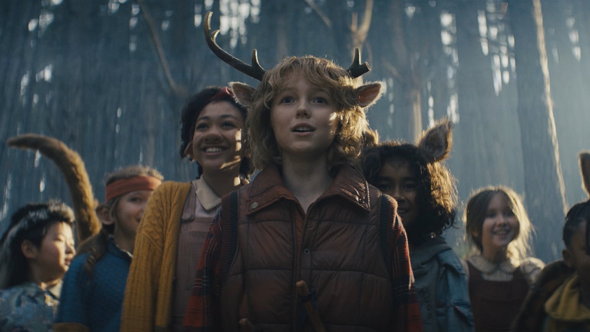 A group of hybrid human-animal children stand in a forest with the light behind them.