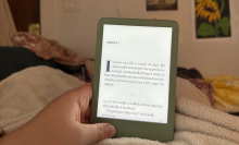 A hand holding a Kindle against a blanket