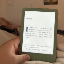 A hand holding a Kindle against a blanket