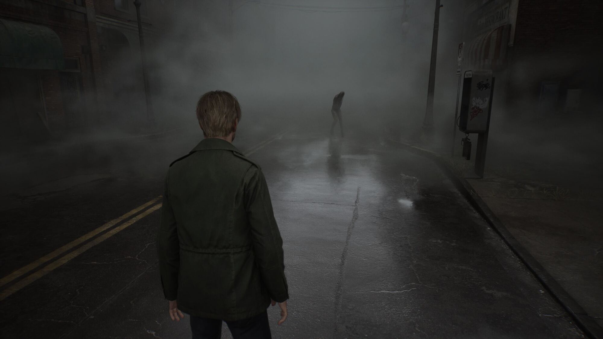 A man with short hair wearing a dark green jacket stands on a foggy street, facing away from the viewer. The street is wet, reflecting the surrounding lights, and an eerie figure appears in the distance, hunched over in a threatening stance. The scene is shrouded in thick fog, creating a haunting and ominous atmosphere