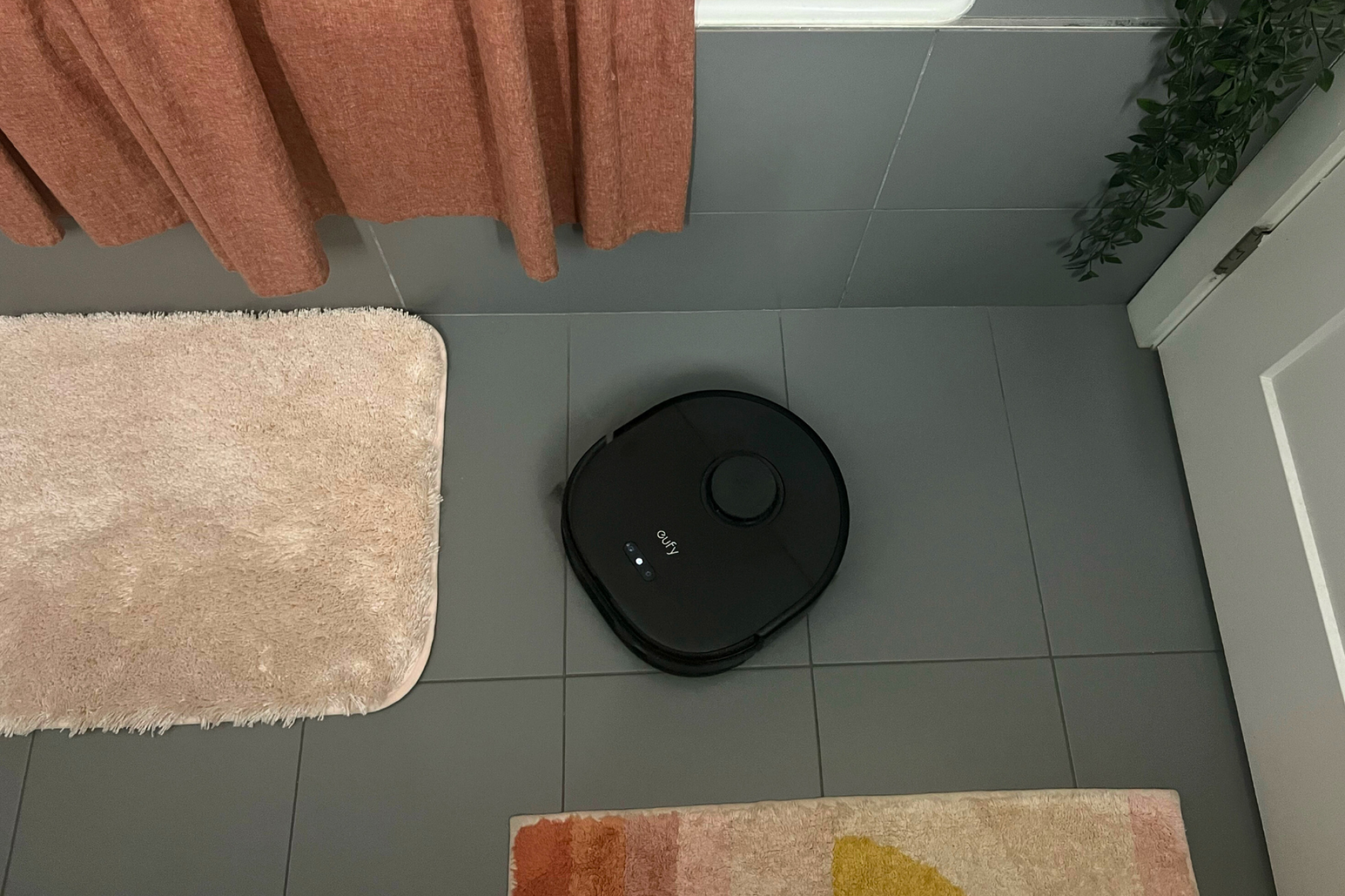 Eufy robot vacuum cleaning tile floor near bath mats with shower and door in peripherals