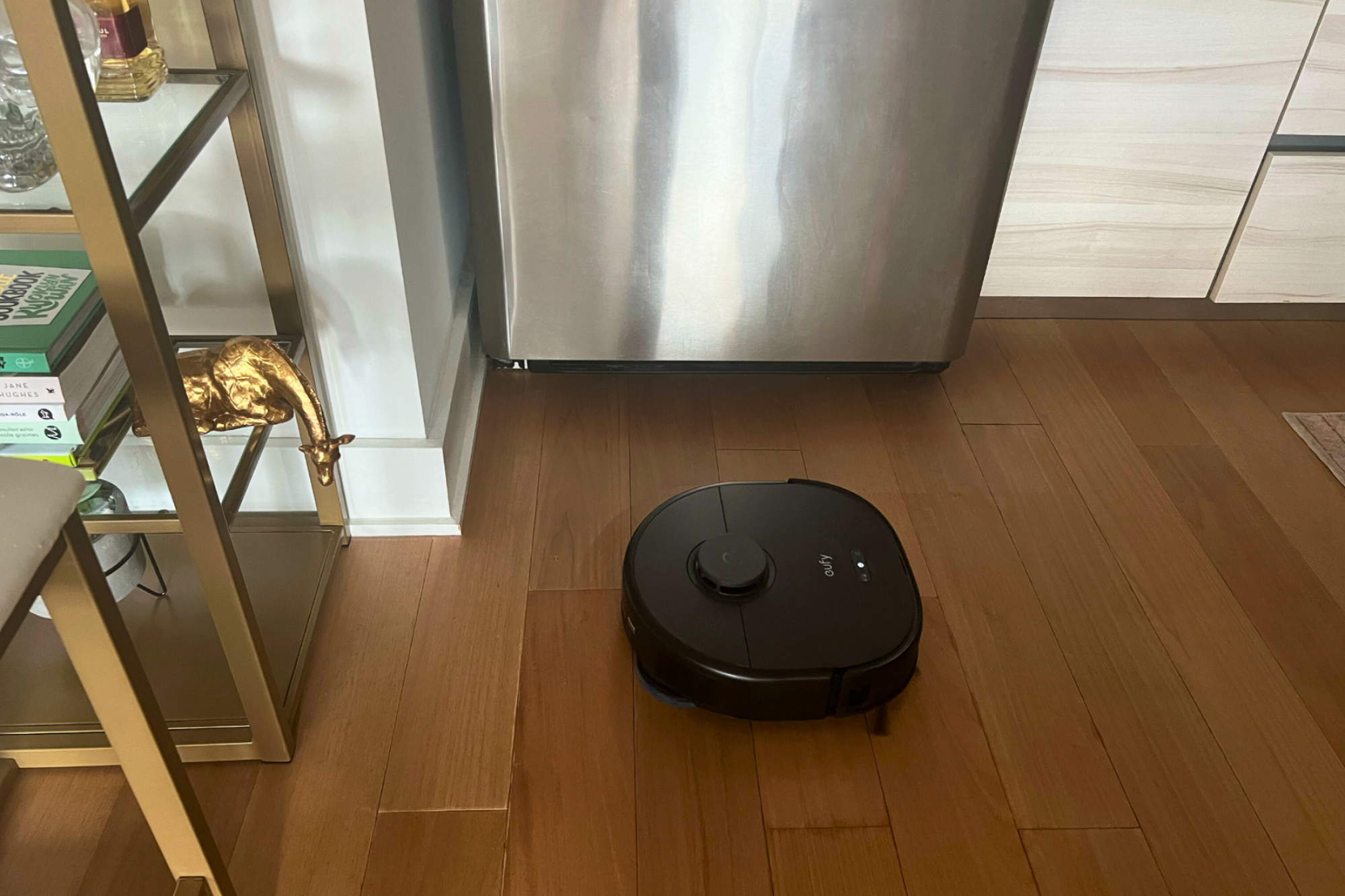 Eufy robot vacuum mopping hardwood floor with kitchen island, refrigerator, and cabinets in peripherals