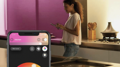 The Philips compatible app shown on a phone next to a woman standing in an LED-lit kitchen