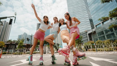 Four women laughing and hugging outside while wearing roller skates