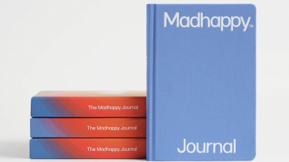 The Madhappy Journal in a blue color standing upright next to a horizontal stack of such journals