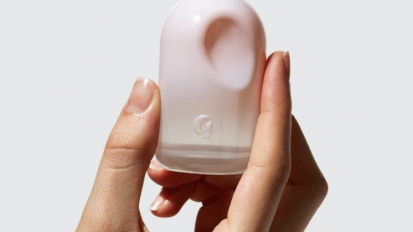 A hand model holding up the pinkish and red Glossier You perfume bottle