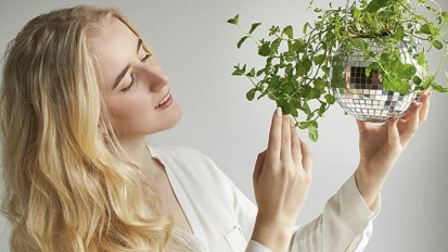 A woman with long blonde hair holding up a plant inside a disco ball planter