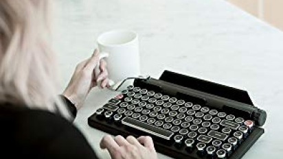 person using black typewriter and holding white mug in other hand