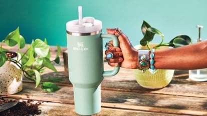 Someone holding out a light blue Stanley Quencher tumbler over a wooden table with plants on it