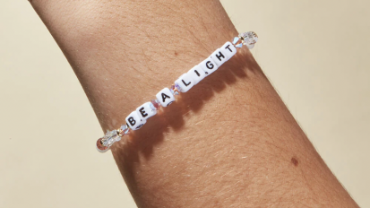 A Little Words Project bracelet with the phrase "Be A Light" on it, worn on someone's wrist