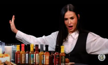 A woman throws her arms wide while sitting in front of a table covered in sauce bottles.