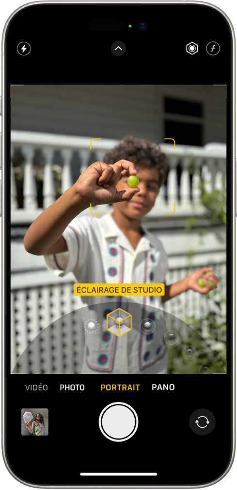L’écran Appareil photo en mode Portrait ; dans le viseur, le sujet est net et l’arrière-plan flou. Le cadran permettant de sélectionner « Éclairage de portrait » est ouvert en bas du cadre et « Éclairage de studio » est sélectionné. Le bouton Flash se trouve en haut à gauche de l’écran, le bouton « Commandes de l’appareil photo » en haut au milieu, et les boutons permettant d’ajuster la profondeur de champ ainsi que l’intensité de l’éclairage de portrait en haut à droite. En bas de l’écran, de gauche à droite, se trouvent le bouton « Visualiseur de photos et vidéos », le bouton « Prendre une photo » et le bouton « Sélecteur de caméra - face arrière ».
