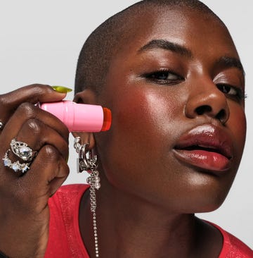 a person holding a pink object close to their ear adorned with various rings and accessories