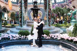 a bride in a white suit and a bride in a black suit pose at the bellagio in las vegas