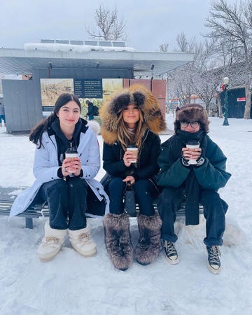 three individuals sitting on a bench in a snowy outdoor environment each holding a beverage