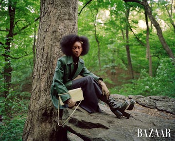 model sits on rick in the woods wearing a green blazer and carrying a bag