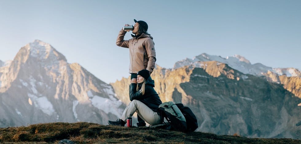 a man taking a picture of a woman sitting on a mountain