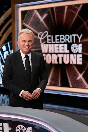 pat sajak smiling for a photo in front of the wheel of fortune logo