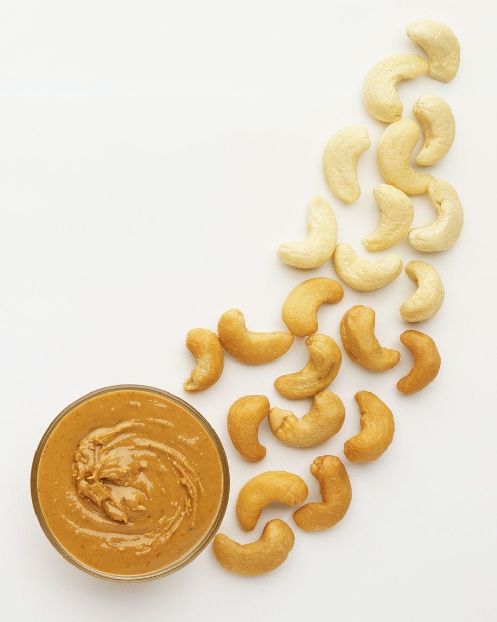 above view of scattered cashew nuts, going from light to dark, toward a jar of swirled cashew butter