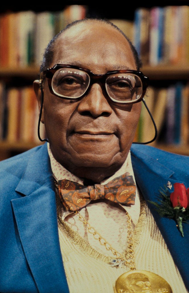 james van der zee wearing stringed glasses and taking a photo in front of bookshelves in the background