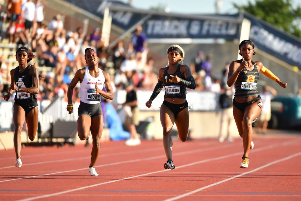 four women run on a track while wearing skintight running uniforms and bibs with their names on them