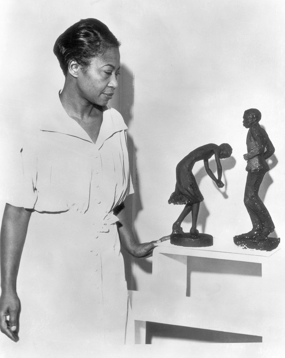 augusta savage resting her left hand on a table as she looks at two of her sculptures