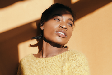 azelaic acid for skin   photo description a young black woman with smooth, bright skin standing in sunlight against a wall