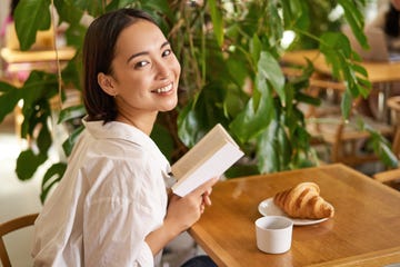 beautiful young asian woman with a book in hands,sitting in cafe