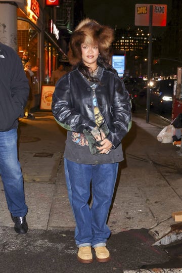 a person wearing a black leather jacket and jeans stands outdoors at night