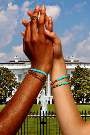 two hands of different skin tones are raised together in front of a historic building