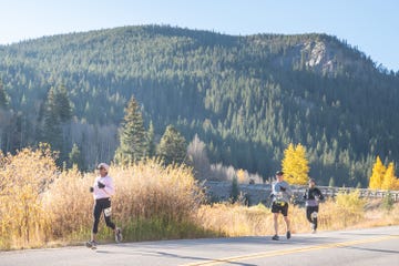 a group of people running on a road with trees and mountains in the background