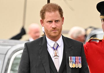 prince harry walking as a guard holds an umbrella for him