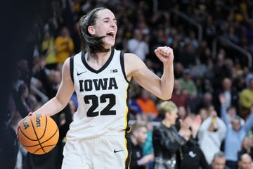 caitlin clark holds a basketball in one hand and pumps her other fist, she wears a white and black basketball uniform for iowa and smiles