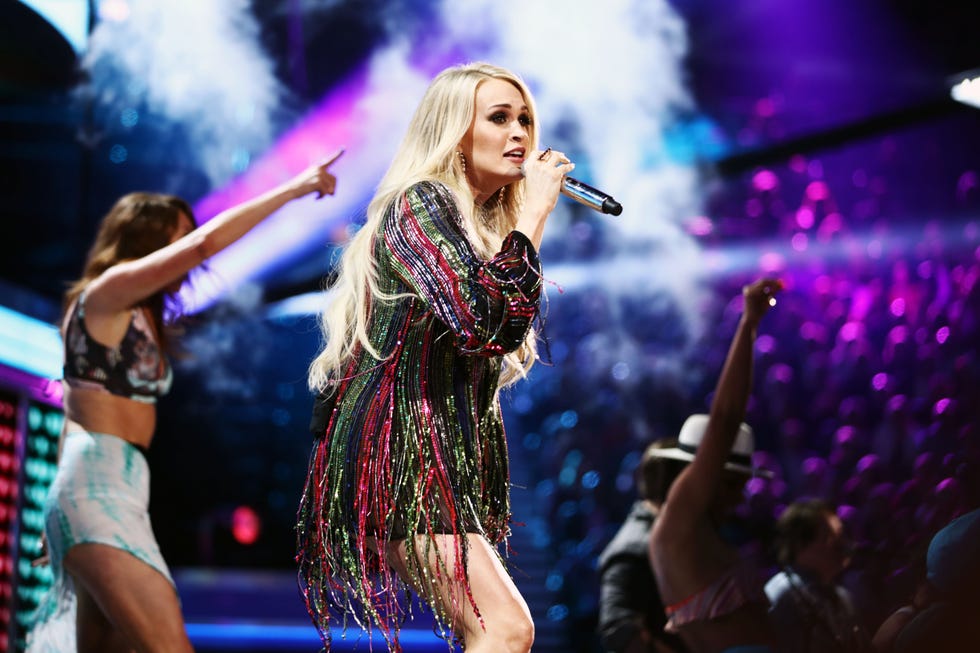 carrie underwood looking out into the crowd as she holds a microphone during her performance