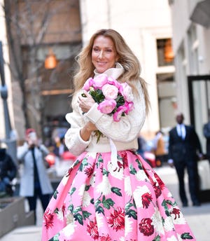 celine dion holding a bouquet of flowers and smiling while walking through new york city