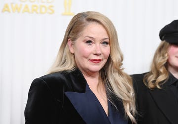 christina applegate smiles at the camera, she wears a velvet blazer and stands in front of a white background