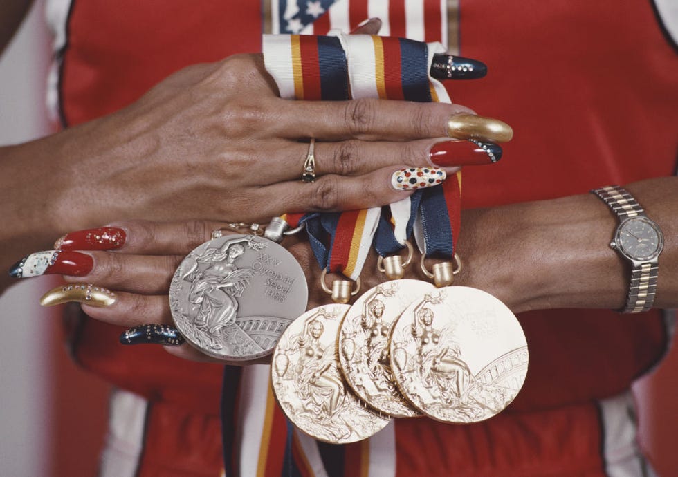 florence joyners hands hold four medals on red, white, blue and yellow striped ribbons, her long nails are bejeweled and painted several colors