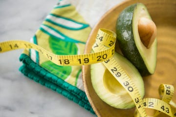 close up of halved avocado, measuring tape and napkin on plate