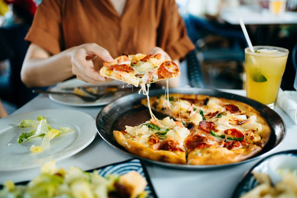 close up of young asian woman getting a slice of freshly made pizza enjoying her meal in restaurant italian cuisine and culture eating out lifestyle