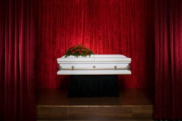 coffin on stage with red flowers on top and dramatic red curtains in the background