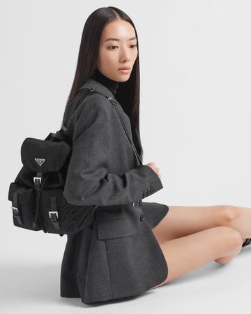 a model wearing a tailored gray blazer and a black backpack seated on the floor