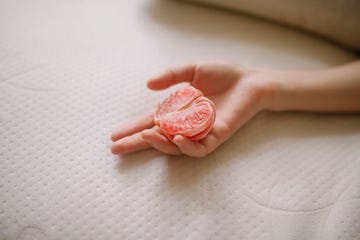 cropped hand of woman holding grapefruit on bed at home