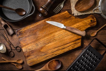 cutting board surrounded by kitchen utensils on a rustic wooden table