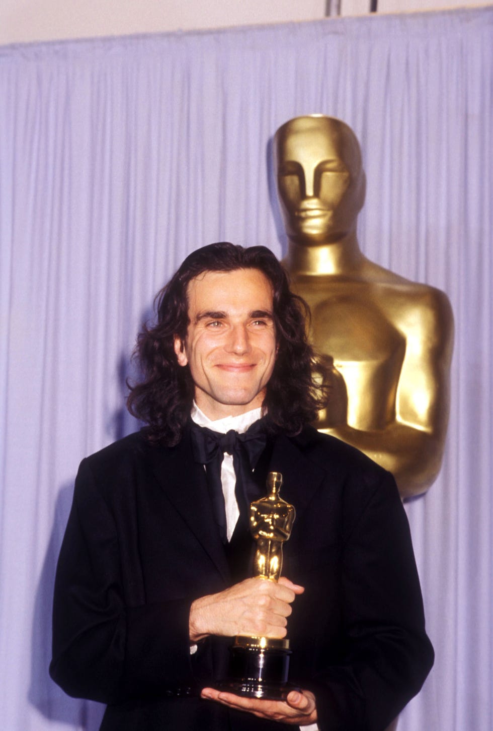 daniel day lewis standing in front of a giant oscar statue and holding a trophy