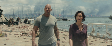 a man and woman standing on a beach with boats in the background